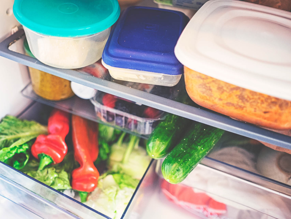 Blick in einen Kühlschrank mit Aufbewahrungsbehältern und frischem Gemüse.